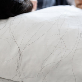 Person lying on a white mattress with a blurred background and a lot of hairs on pillow.